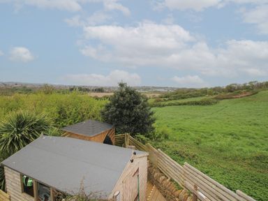 A backyard with a wooden shed and gazebo overlooking green fields under a cloudy sky at Blue Waters in Weymouth