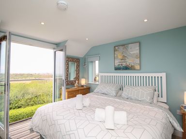 A bedroom with a double bed next to an open door and a wooden dresser with a mirror at Blue Waters Weymouth
