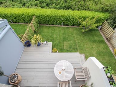 A backyard with a wooden deck table and chair a small grass lawn and plants at Blue Waters in Weymouth
