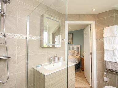 A bathroom with a shower, sink, mirror, and towels with a bedroom visible through an open door at Blue Waters in Weymouth