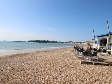 A pebble beach with tables and chairs on a wooden deck next to a building at Blue Waters in Weymouth
