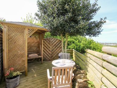 An outdoor wooden seating area with a round table and chairs under a tree near a wooden fence at Blue Waters in Weymouth