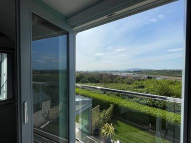 A view through a glass door showing a garden hedge rooftops and water beyond at Blue Waters in Weymouth
