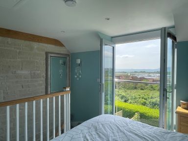 A bedroom with a bed near an open balcony door overlooking greenery and water at Blue Waters in Weymouth