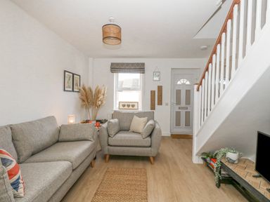 A living room with two grey sofas a window and a front door near stairs at The Nightingale in Weymouth