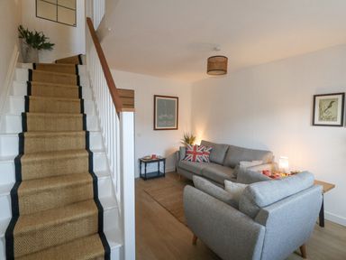 A living room with grey sofas and a staircase with a carpet runner at The Nightingale in Weymouth