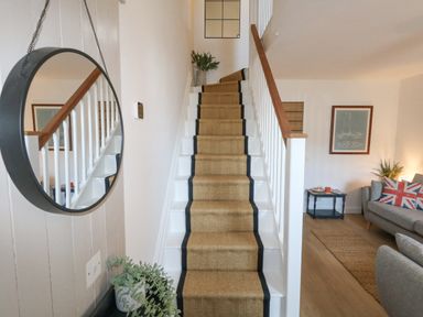 A staircase with a carpet runner and a round mirror on the wall next to a living room with a sofa and side table at The Nightingale in Weymouth