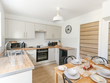 A kitchen with wooden countertops and white cabinets next to a dining table set with bowls and glasses at The Nightingale in Weymouth