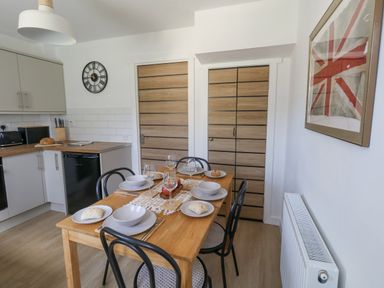 A kitchen dining area with a wooden table set with plates glasses bread and a centerpiece with four chairs near wooden doors at The Nightingale in Weymouth
