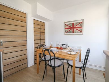 A dining area with a wooden table set for four with black chairs and a framed union jack on the wall at The Nightingale in Weymouth