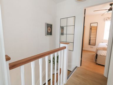 A stairway with wooden handrail and white spindles leading to a bedroom with a bed ceiling fan and a full-length mirror at The Nightingale in Weymouth