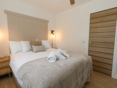 A bedroom with a bed made with white and beige bedding plus rolled towels and a wooden door at The Nightingale in Weymouth