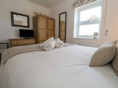 A bedroom with a bed with white linens and rolled towels a wooden dresser wardrobe a wall mirror and a window at The Nightingale in Weymouth