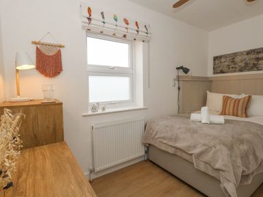 A bedroom with a bed by a window a wooden dresser with a lamp and decorative items at The Nightingale in Weymouth