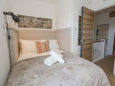 A bedroom with a bed with pillows a blanket rolled towels on the bed a desk lamp and an open door at The Nightingale in Weymouth