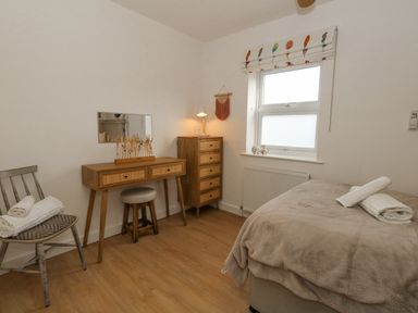 A bedroom with a bed, wooden dresser, chair with towels, and a window at The Nightingale in Weymouth