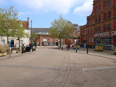 A pedestrian street with trees benches and people near brick buildings at The Nightingale in Weymouth