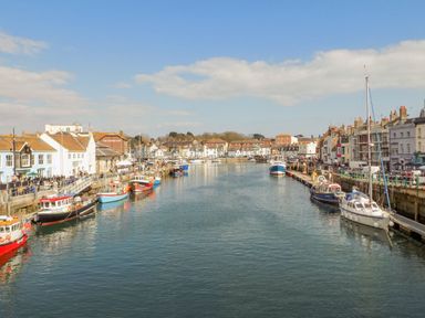 A harbor with boats docked along both sides and buildings lining the waterfront at The Nightingale in Weymouth