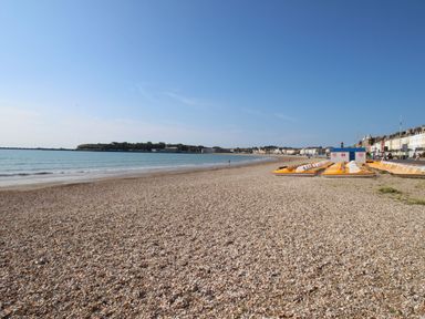 A pebble beach with yellow pedal boats lined up by the shore and buildings along the coast at The Nightingale in Weymouth