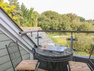 A small balcony with a round metal table and two chairs with cushions overlooking trees and a sports court at 5 Court Cottage Hillfield Village in Dartmouth