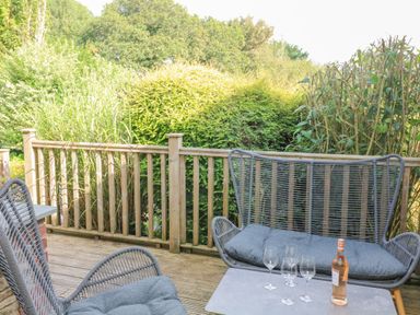 An outdoor wooden deck with a table and chairs surrounded by greenery at 5 Court Cottage Hillfield Village in Dartmouth