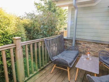 An outdoor wooden deck with a gray cushioned bench chairs a table with a bottle and glasses at 5 Court Cottage Hillfield Village in Dartmouth