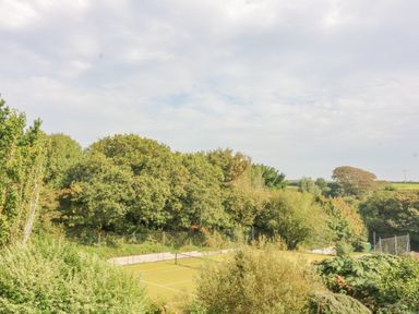 A tennis court surrounded by trees and greenery at 5 Court Cottage Hillfield Village in Dartmouth