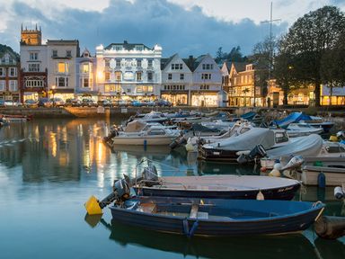 A harbor with multiple boats docked on calm water and a row of buildings with lights on in the background at 5 Court Cottage Hillfield Village in Dartmouth