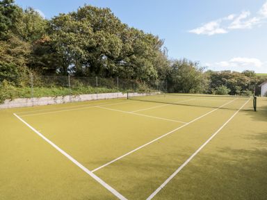 An outdoor tennis court with a net and surrounded by trees at 5 Court Cottage Hillfield Village Dartmouth