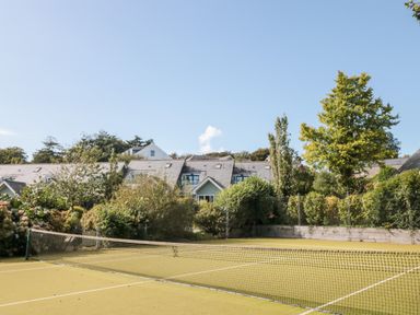 An outdoor tennis court with a net surrounded by trees and houses at 5 Court Cottage Hillfield Village in Dartmouth