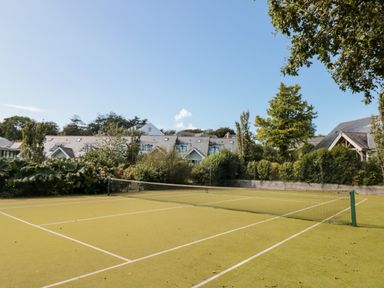 A tennis court with a net surrounded by trees and houses at 5 Court Cottage Hillfield Village in Dartmouth