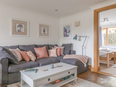 A living room with a grey sofa with pink and striped cushions and a white coffee table next to a bedroom at 5 Court Cottage Hillfield Village Dartmouth