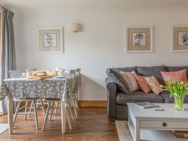 A dining table with polka dot tablecloth and breakfast items next to a sofa with cushions and a coffee table with flowers at 5 Court Cottage Hillfield Village in Dartmouth