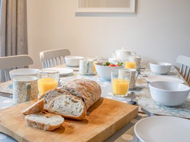 A dining table set with bread on a cutting board bowls cups glasses of orange juice and a bowl of fruit at 5 Court Cottage Hillfield Village in Dartmouth