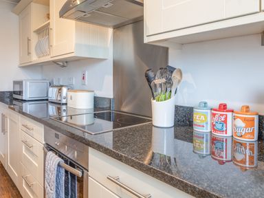 A kitchen countertop with utensils in a holder containers for tea coffee and sugar a toaster microwave and stove at 5 Court Cottage Hillfield Village Dartmouth