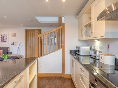 A kitchen with white cabinets black countertops and wooden stairs at 5 Court Cottage Hillfield Village in Dartmouth