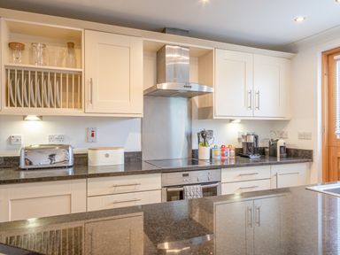 A kitchen with white cabinets black countertops a toaster a bread box cooking utensils and a coffee machine at 5 Court Cottage Hillfield Village Dartmouth