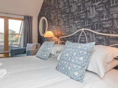 A bedroom with a double bed blue patterned pillows an armchair lamp and balcony doors at 5 Court Cottage Hillfield Village in Dartmouth