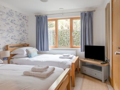 A bedroom with two single beds a television on a stand and a window with curtains at 5 Court Cottage Hillfield Village in Dartmouth