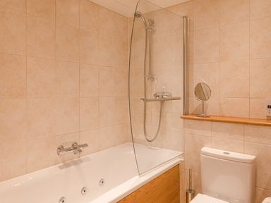 A bathroom with a bathtub and shower, a toilet, and a small round mirror on a shelf at 5 Court Cottage, Hillfield Village in Dartmouth