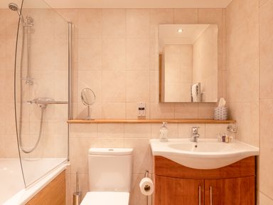 A bathroom with a bathtub shower combination a toilet and a sink with wooden cabinets at 5 Court Cottage Hillfield Village Dartmouth