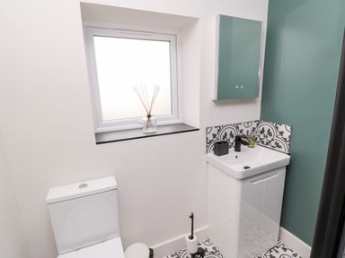 A bathroom with a toilet a sink cabinet patterned tiles and a frosted window at Nene's Nest in Alnwick