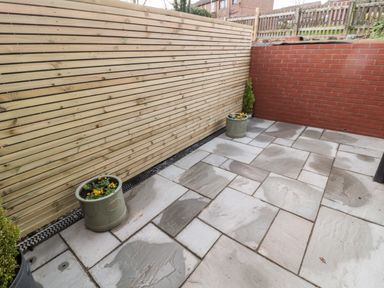 A small patio with stone tiles wooden fence on one side and brick wall on the other with potted plants at Nene's Nest in Alnwick