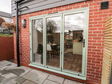 A brick exterior wall with a set of green framed glass patio doors leading to a room with a dining table and chairs at Nene's Nest in Alnwick