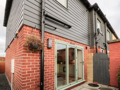 Exterior view of a house with red brick lower walls gray siding upper walls green framed glass door and gate at Nene's Nest in Alnwick