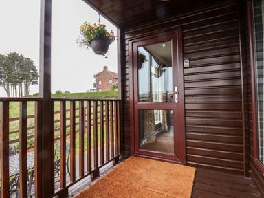 A wooden balcony with a glass door a hanging flower pot and outdoor table and chairs at Handale Banks Farm Lodge in Liverton