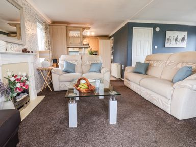 A living room with two beige sofas a glass coffee table with a fruit bowl and a fireplace at Handale Banks Farm Lodge in Liverton