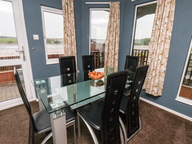 A dining room with a glass table surrounded by six black chairs and curtains on windows at Handale Banks Farm Lodge in Liverton