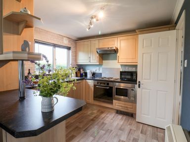 A kitchen with wooden cabinets a black countertop an oven microwave kettle flowers in a jug and a window at Handale Banks Farm Lodge Liverton