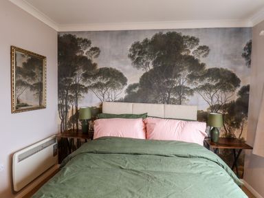 A bedroom with a bed green bedding and pink pillows two wooden side tables with green lamps and forest mural on the wall at Handale Banks Farm Lodge Liverton